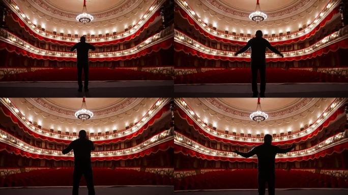 舞台上演员的后视图。男子在红色椅子的空荡荡的礼堂里用手势练习演讲。表演者是剧院的重头戏。