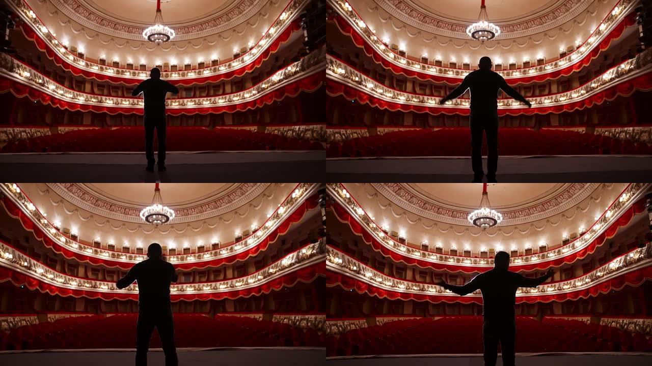 舞台上演员的后视图。男子在红色椅子的空荡荡的礼堂里用手势练习演讲。表演者是剧院的重头戏。