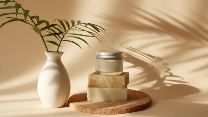 在阳光下，米色讲台上的玻璃罐中的奶油来自肥皂条。阴影棕榈叶。产品展示的最小抽象化妆品背景。产品展示