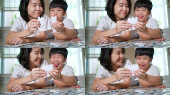 亚洲家庭，母子俩躺在地板上拿着拼图并将它们放在一起。在家工作期间家庭幸福。女人教孩子解谜。父母和开朗