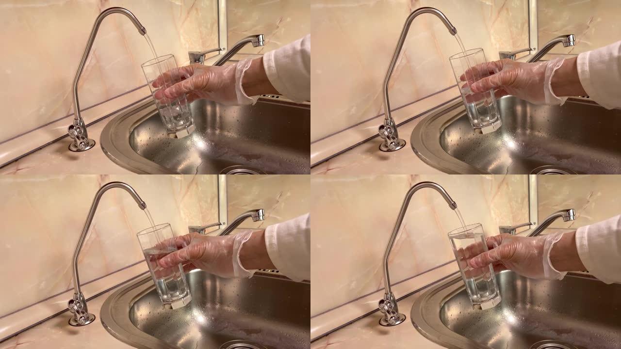 将过滤水从滤水器倒入玻璃中。水槽和水龙头的特写。厨房里的饮用水