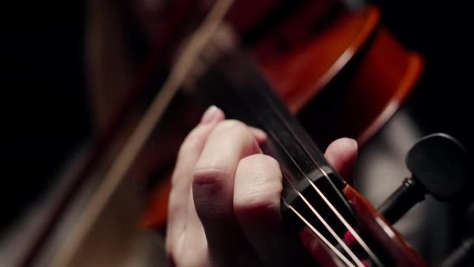 一位女小提琴手手中的小提琴琴颈的特写镜头，在黑暗中用琴弦演奏弓