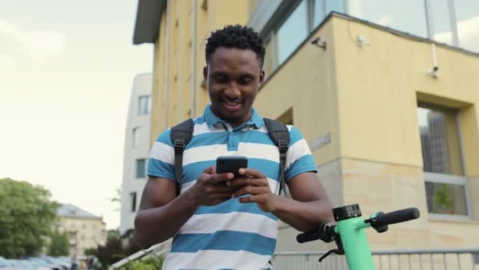 美国黑人男子使用智能手机支架和电动滑板车。生态交通。城市户外。