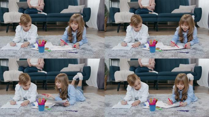 儿童休闲概念，可爱的微笑友好的12岁男孩和女孩在地板上放松，用毡尖笔画画，而他们的母亲坐在沙发上，在