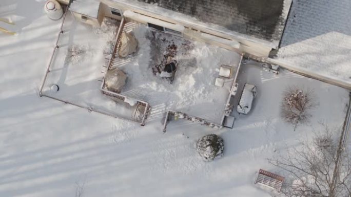 一名成年男子在冬季降雪后用铁锹从雪地上清理门廊。无人机慢动作视频正上方鸟瞰。