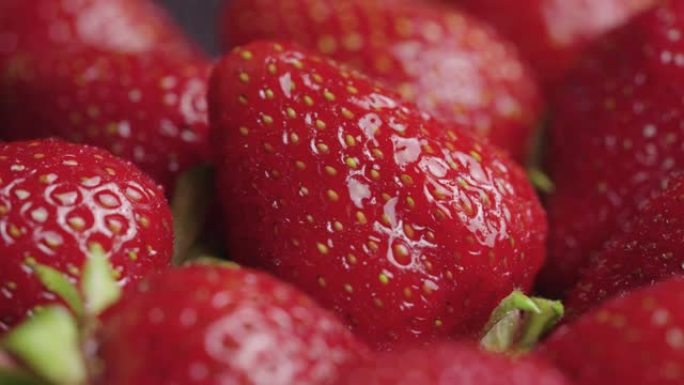 覆盖着水滴的多汁成熟草莓靠近旋转。夏季甜浆果，绿色尾巴。健康的有机素食食品。维生素健康水果