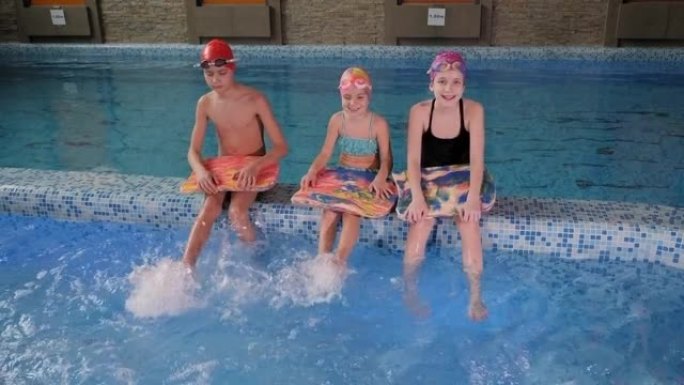 室内游泳池中戴游泳帽的三个小孩的肖像。