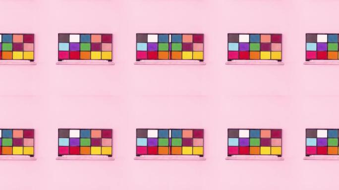 由许多不同颜色的眼影调色板制成的创意图案在明亮的粉红色主题上旋转。停止运动