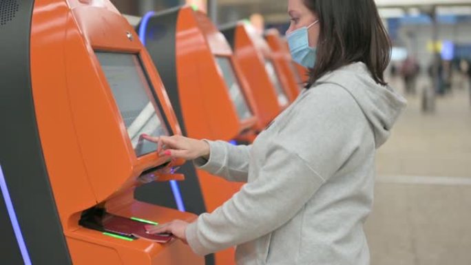 妇女在机场自助办理登机手续。妇女使用售票亭机戴着防护口罩旅行，在机场航站楼自助办理登机手续，在线订票