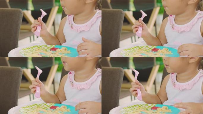 特写4k无法辨认的可爱的亚洲3岁宝宝正在吃，咀嚼和坐在椅子上作为早餐，用肮脏的手和嘴。她看起来饿了，