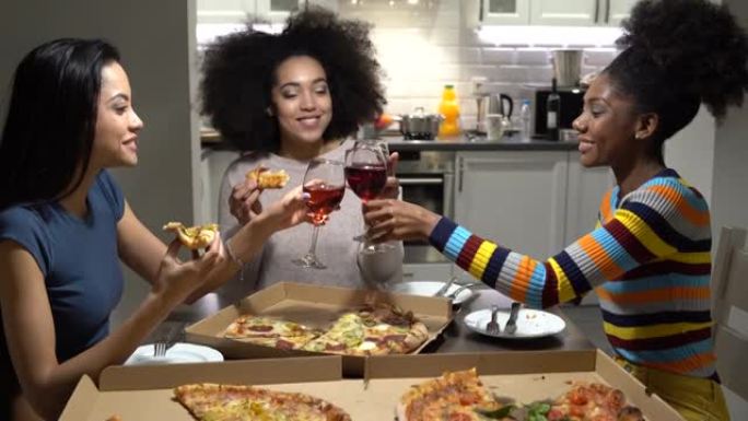 4k视频快乐多种族的三个年轻女人坐在厨房里，吃披萨，喝葡萄酒，开玩笑和大笑
