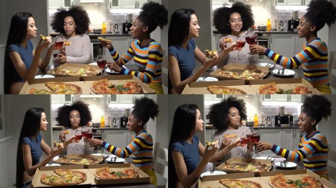 4k视频快乐多种族的三个年轻女人坐在厨房里，吃披萨，喝葡萄酒，开玩笑和大笑