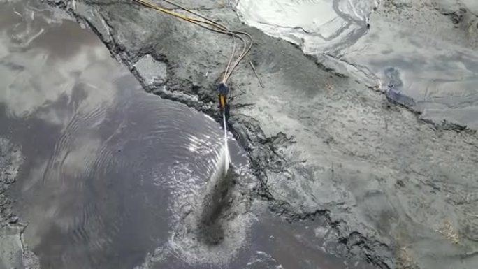 工人用一大股水流冲走土壤。用高压水冲洗土壤。压力下的水从软管中流出。冲积废水残留物