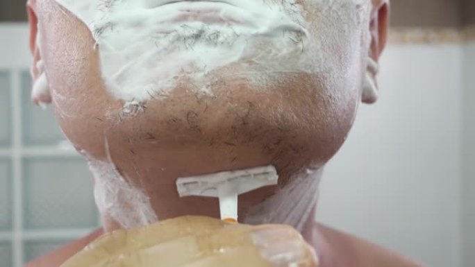无法识别的男人用橙色剃须刀在脸上刮泡沫