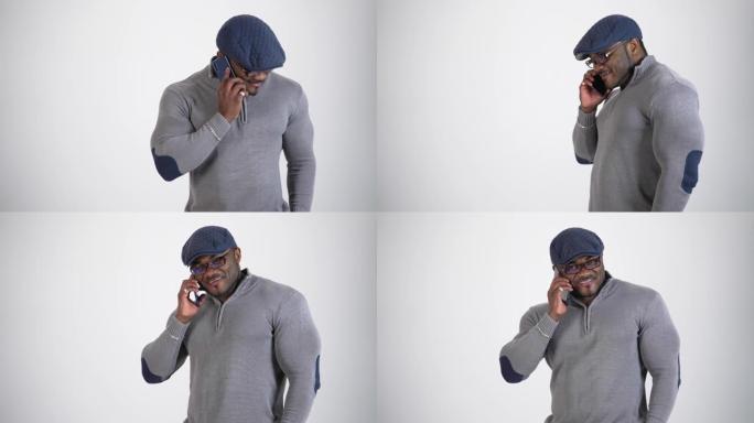 微笑的黑人皮肤男子打电话。快乐的非洲年轻人戴着眼镜和帽子在演播室里用白色孤立的电话交谈。