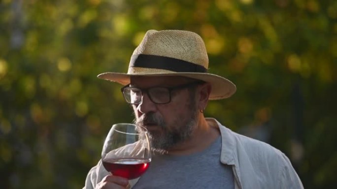 一个成熟的人在葡萄园外面品尝葡萄酒的镜头。