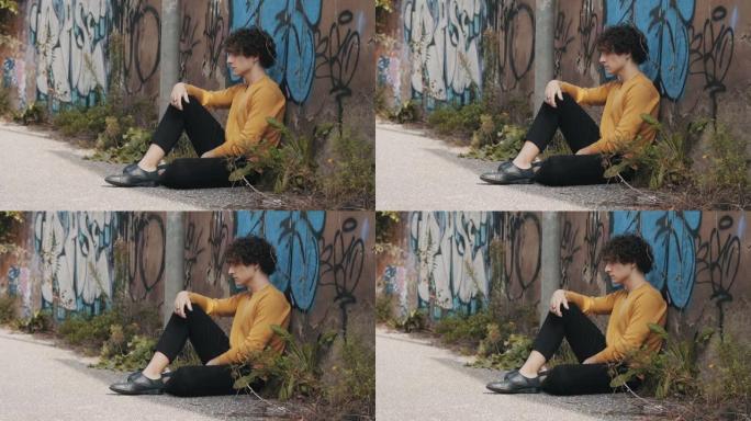 冷漠，沮丧-年轻的悲伤男人坐在街上的地面上思考