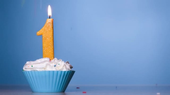 柔和蓝色背景上燃烧的彩色蜡烛一号生日蛋糕。120 FPS。带复制空间的慢动作周年横幅。