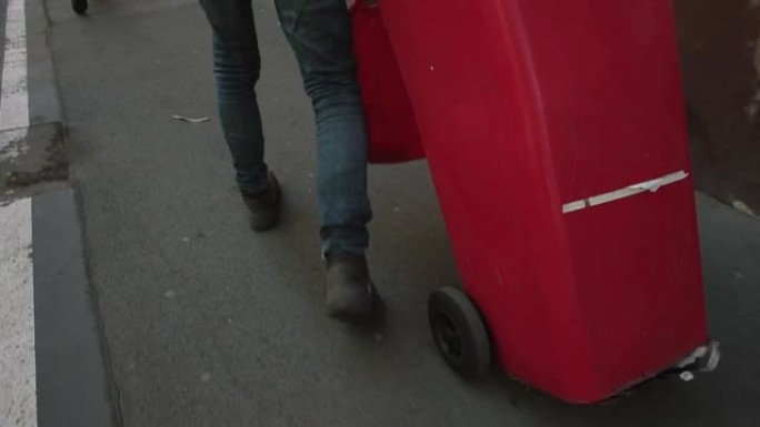 一个人腿的运动，一个红色的垃圾桶。城市中的废物收集