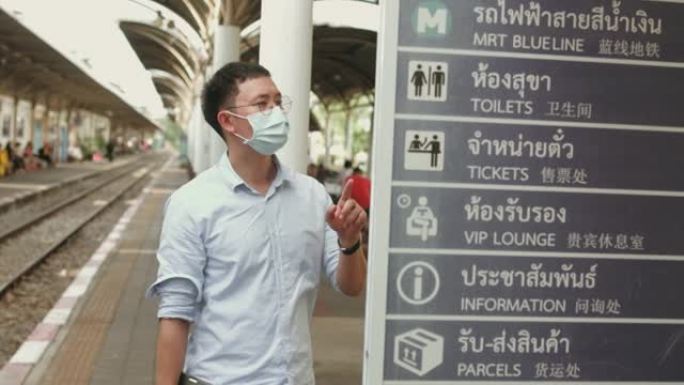 在新冠肺炎期间，一名戴口罩的亚洲男子检查到离站板等待列车