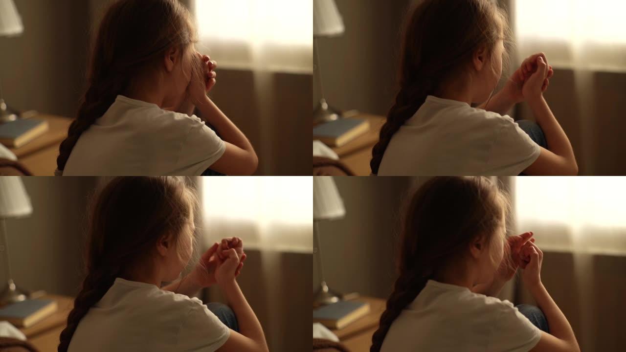 沮丧的小女孩独自坐在窗户背景上的床上哭泣的特写镜头。