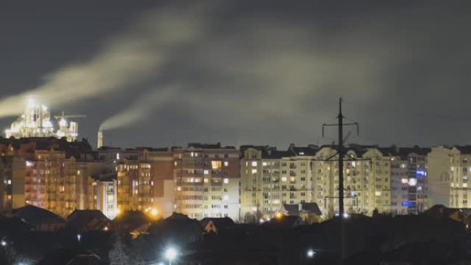 城市住宅区的高层公寓楼和高大的工厂烟囱，晚上远处冒烟。