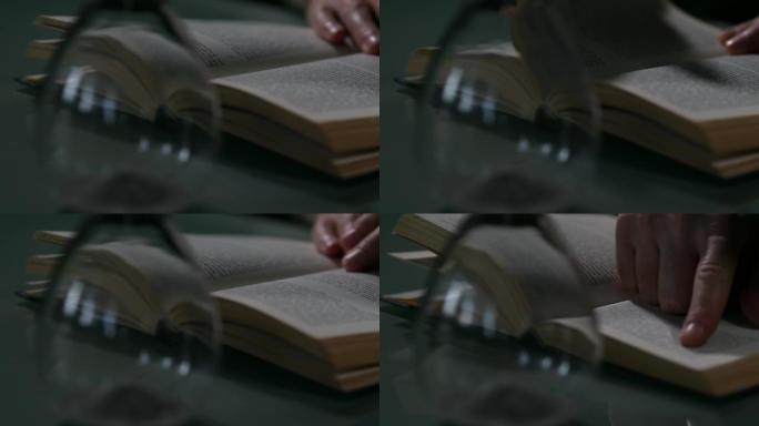 人的手转动一本旧书的书页。当时的书和沙漏。哥特式氛围。绿色玻璃桌子背景