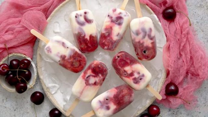 新鲜奶油和樱桃自制冰棍放在白色陶瓷盘上，配有水果和纺织品