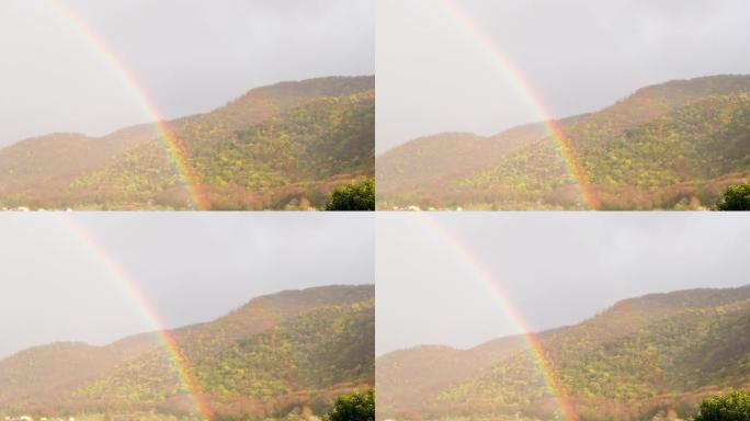 惊人的彩虹出现在阳光下的天空和山脉背景上，下雨后出现自然现象，而阳光普照。多色光谱，抽象想象，形成