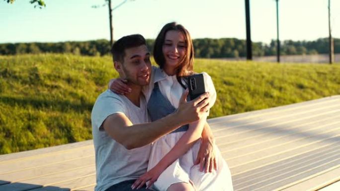 周末散步时，在夏季城市公园的长凳上坐在手机上视频通话的快乐情侣的肖像。