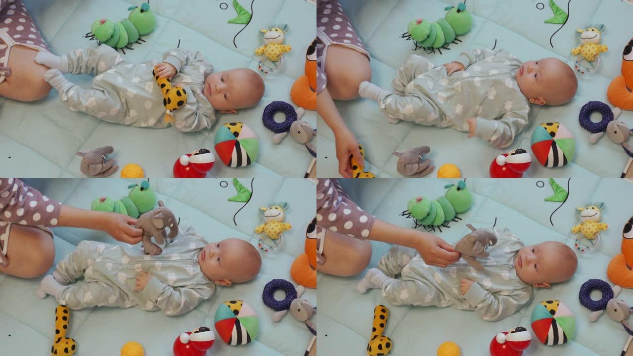 妈妈和宝宝在一起玩得开心坐在家里的地板上，女人和她3个月大的男婴在活动中玩玩具垫子