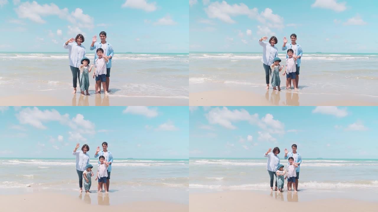 家庭时间的父母和孩子站在摄像机前微笑着，在早晨的阳光下在海滩上挥舞着双手。