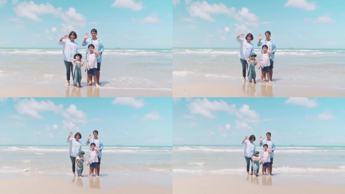 家庭时间的父母和孩子站在摄像机前微笑着，在早晨的阳光下在海滩上挥舞着双手。
