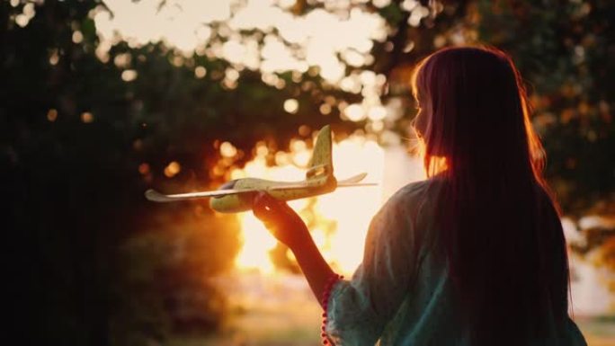 一个孩子在日落时玩飞机，一个女孩在橙色的阳光下的轮廓