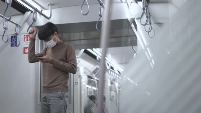 年轻的亚洲男子乘客戴着防护口罩，在空中火车上使用电话拿着手环