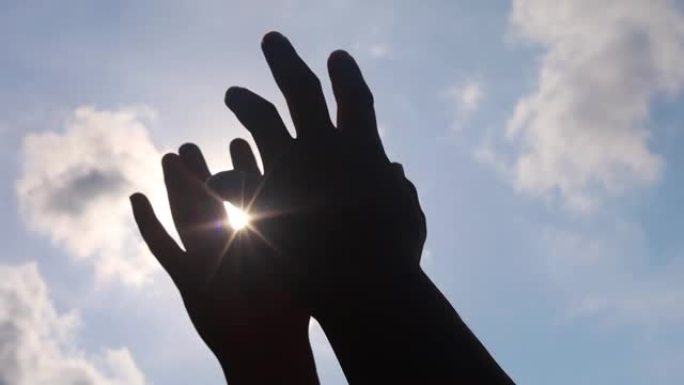 在蓝天背景上，人的双手与太阳光一起玩耍。