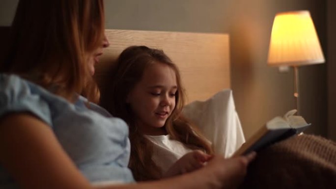 睡觉前，快乐的年轻母亲和可爱的女儿一起阅读儿童书的特写肖像。