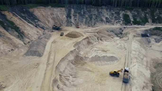 前端装载机在露天矿将沙子装载到自卸车中。颚式破碎机制砂生产线。在采石场工作的重型采矿机械。