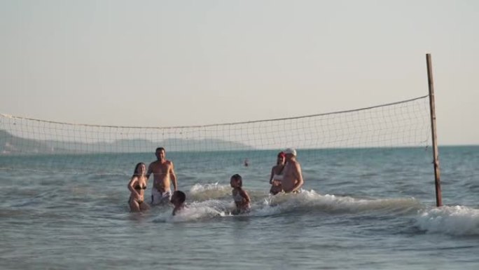 一群年轻人在日落时在热带海滩上打排球进入大海