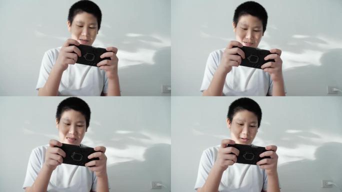 亚洲男孩坐在地板上玩手机游戏，家里有阳光阴影，生活方式概念。