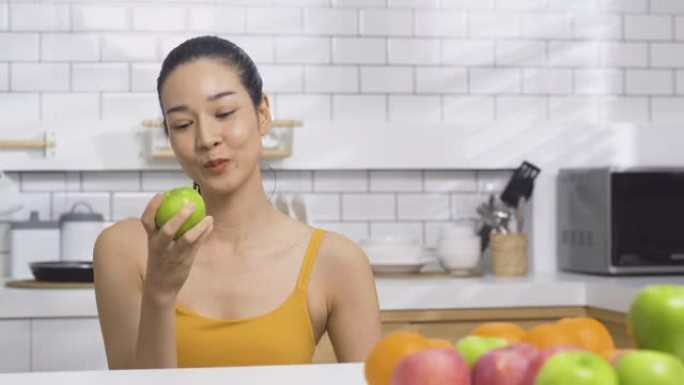 美丽的女人在厨房吃青苹果。