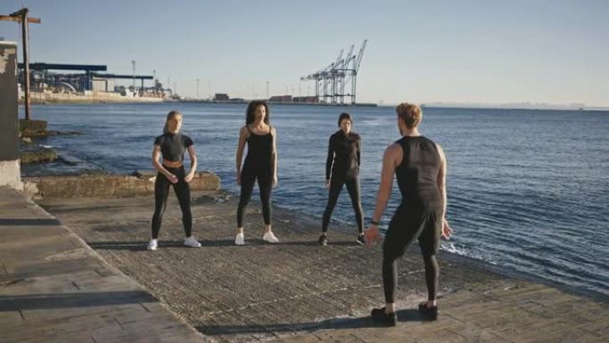 积极的户外训练。三名年轻的女性在码头蹲下，在码头上与团体健身教练一起训练