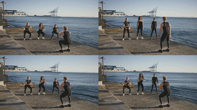 积极的户外训练。三名年轻的女性在码头蹲下，在码头上与团体健身教练一起训练