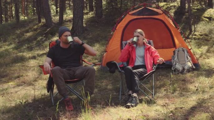 森林露营 -- 年轻的徒步旅行者夫妇在营地享受一杯t恤