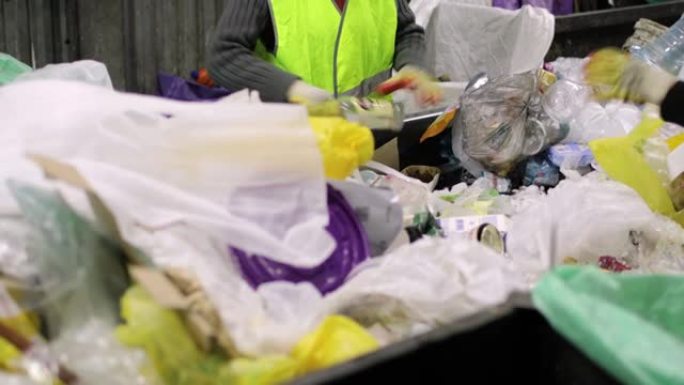 垃圾容器。一堆各种垃圾，塑料，玻璃纸。戴着手套的人正在用手分类垃圾。特写