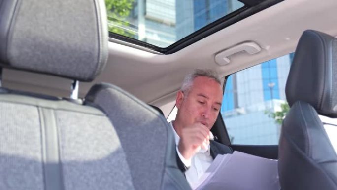 白发苍苍的富商坐在车辆后座上，在网上打电话