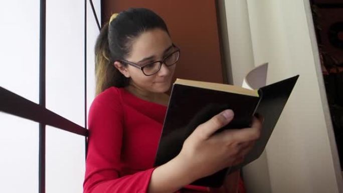 一个可爱的害怕震惊的特写肖像惊讶的年轻少女学生戴着眼镜坐在图书馆靠近窗户，张着嘴看书