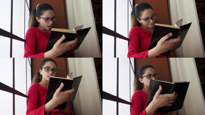 一个可爱的害怕震惊的特写肖像惊讶的年轻少女学生戴着眼镜坐在图书馆靠近窗户，张着嘴看书