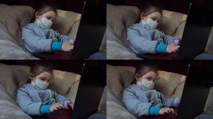 戴着医用面具的可爱的孩子在检疫的扶手椅上使用笔记本电脑学习