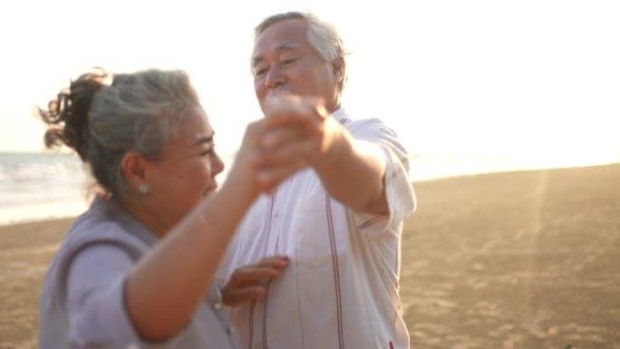亚洲老年夫妇喜欢在夏日日落时在海滩上跳舞和浪漫的假期